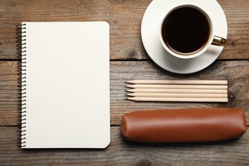 Blank sketchbook, coffee, pencils and case on wooden table, flat lay