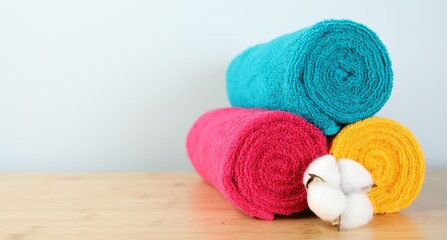 Colorful fresh terry towels and cotton flower on wooden table, closeup. Space for text