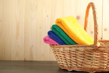Colorful fresh terry towels in basket on wooden table, closeup. Space for text