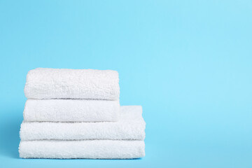 Stack of white towels on light blue background, closeup. Space for text