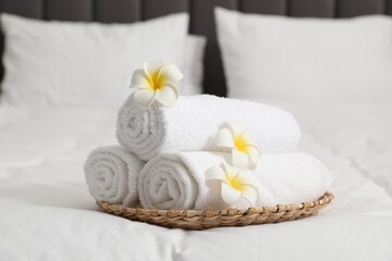 Rolled white towels and plumeria flowers on bed, closeup