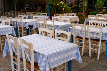 Close-up of tables and chairs with tablecloths in a Greek tavern. Traditional dining setup, cozy coastal restaurant atmosphere, perfect for travel or food content