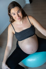 Vertical picture of a pregnant woman doing exercises with pilates ball at home