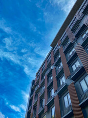 Obraz premium Modern hotel building captured from a low angle with a clear blue sky and clouds in the background, showcasing contemporary architecture and urban design.