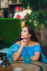 Young woman with colorful makeup enjoys a drink at a vibrant outdoor cafe in warm weather