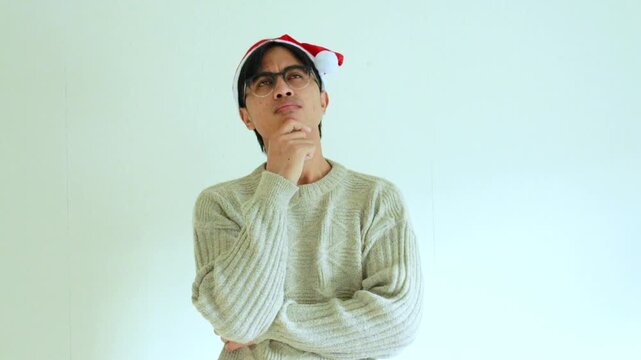 Serious young man in Santa hat with Christmas accessories making a thinking gesture in studio, perfect for holiday themes, winter celebration, and festive concept videos.