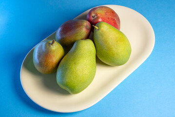 green and red pears on a yellow plate isolated on blue background, organic vegetarian food, fruit