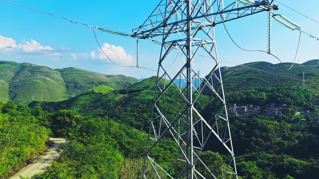 Aerial shot of a high voltage electricity transmission tower and power lines set against a backdrop of lush green rolling hills.