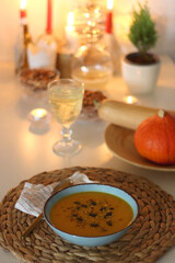 Plate of pumpkin soup, pumpkins, glass of wine, nuts and lit candles on the table. Selective focus.