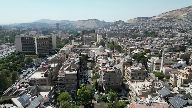 An aerial view captures the new Syrian national flag hoisted on a towering pole in central Damascus, with Mount Qasioun, one of the capital&rsquo;s most prominent landmarks rising in the background.