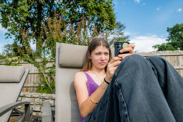 Beautiful young girl using her mobile phone in the garden, appearing to receive bad news