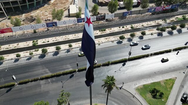 An aerial view captures the new Syrian national flag hoisted on a towering pole in central Damascus, with Mount Qasioun, one of the capital&rsquo;s most prominent landmarks rising in the background.