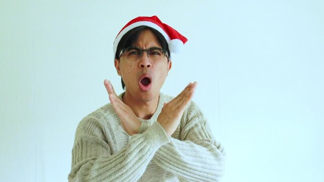 Serious young man wearing a Christmas outfit and Santa hat making a stop hand gesture in a studio festive background, ideal for holiday themes, seasonal messages, and Christmas campaign videos.