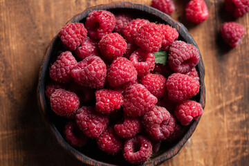 Raspberries in wooden bowl on old wooden table background, closeup view. Summer berry harvest