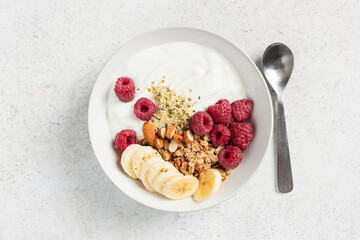 Yogurt bowl with raspberroes, banana and muesli granola on grey table background. Concept of clean eating, dieting, healthy fitness meal