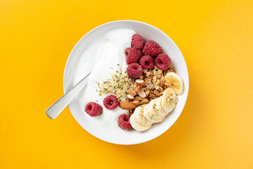 Fruit and berry yogurt bowl with granola on yellow background, healthy meal menu, top view
