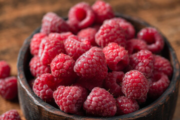 Raspberries in wooden bowl on old wooden table background, closeup view. Summer berry harvest