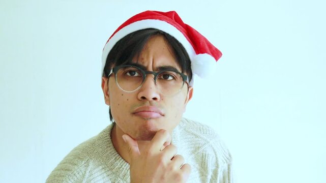 Serious young man wearing a Santa hat and Christmas accessories making a thinking gesture in a studio setting, ideal for holiday themes, winter celebrations, and festive concept videos.