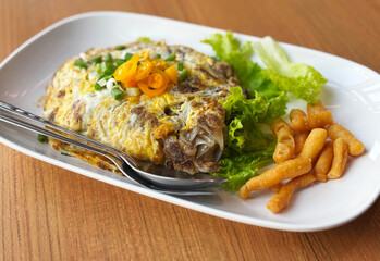 Stir-fried flat noodles with chicken, wrapped with egg. Close up Asian Thai-Chinese food menu on wooden table.