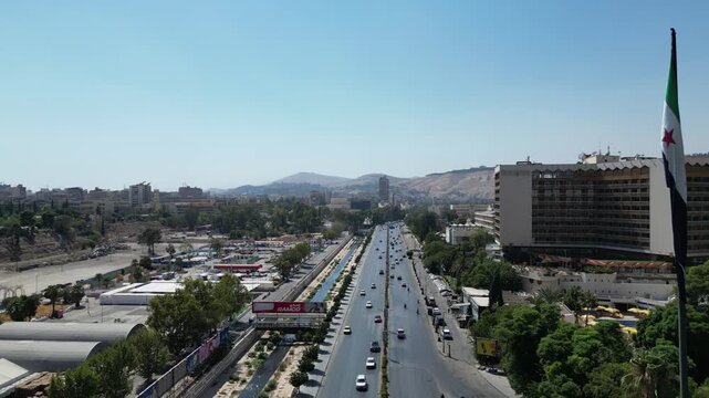 An aerial view captures the new Syrian national flag hoisted on a towering pole in central Damascus, with Mount Qasioun, one of the capital&rsquo;s most prominent landmarks rising in the background.