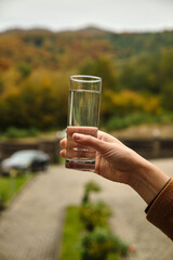 Hand holding a glass of water with a scenic background