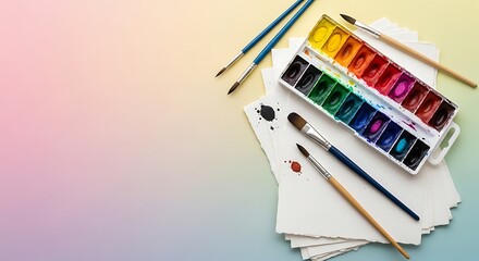 Overhead view of colorful watercolor paints and brushes laid out on a pastel gradient background with copy space