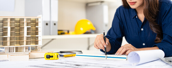 Young female engineer designer or contractor working on drawing plans and making measurements on...