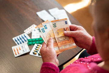 An elderly woman counting euros near medication. A grandmother counts money against a background of medicines, a symbol of the high cost of medicines and the lack of funds in Europe