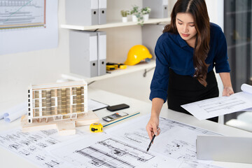 Young asian civil engineer studying a blueprint floor plan and  working with documents, drawings...