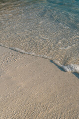Minimal, people-free close-up of a gentle wave with foam over smooth sand and clear shallow water on the Ionian coast in Ksamil, Albania—versatile for travel, wellness and resort branding, with copy s