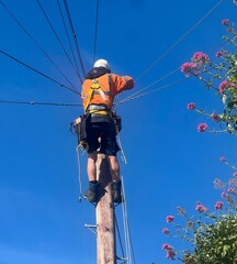 Telecoms engineer working at the top of a telegraph pole on telecommunications, broadband and wiring for homes in a town