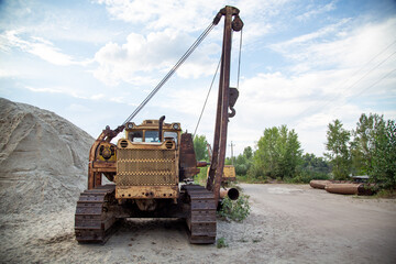 An old pipelayer against the backdrop of pipe sections and a pile of sand washed up by a dredger