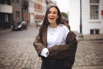 Woman wear trench coat. Portrait of young happy long hair brunette woman on city street looking at...
