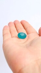 Teal gem held in a light-skinned hand against a white background