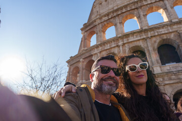 Smiling tourists taking selfie with Colosseum in background during sunny winter day in Rome