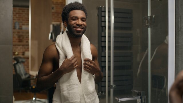 African American ethnic bare man smiling in mirror reflection in bathroom bearded male guy shaving face morning shower hygiene shave facial smooth skin grooming cosmetics moisturize lotion gel cream