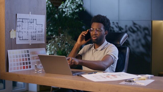 African American business man architect designer talk mobile phone in office businessman overwork night evening online work laptop cellphone call male engineer consulting design architecture project - Powered by Adobe