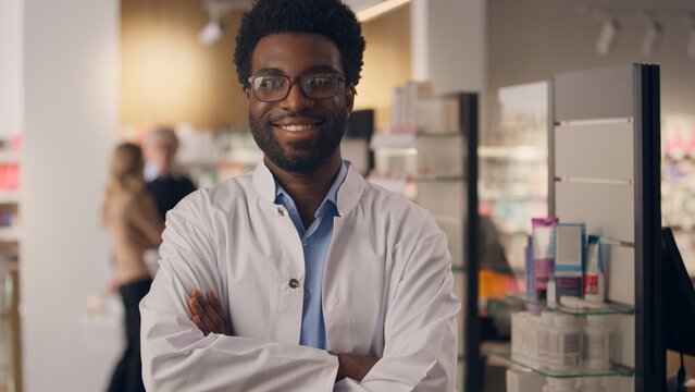 African American ethnic man portrait health care worker doctor pharmacist smiling guy in pharmacy drugstore shelves with medicine male physician seller in medical coat healthy insurance crossed hands - Powered by Adobe