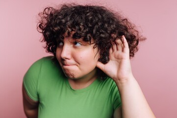 Young person with curly hair and green shirt listening carefully against a pink background