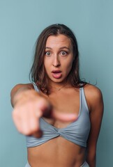 Fototapeta premium Woman looks surprised and points forward against a light blue backdrop indoors during the day