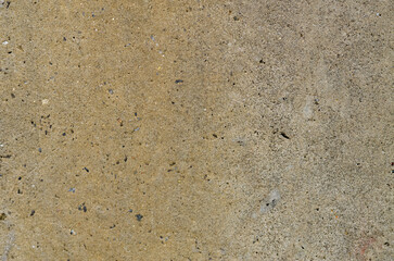 A detailed close-up of a warm, sandy-colored concrete surface, highlighting its porous texture, darker flecks of aggregate, and tiny pits for an industrial background.
