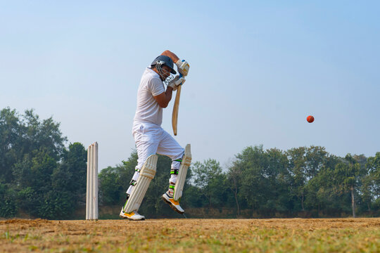 A cricketer in white skillfully dodges a ball on a grassy field, showcasing defensive technique and focus