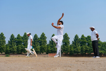 A cricket bowler in action, delivering a ball with focus and precision on a sunny field, watched by teammates