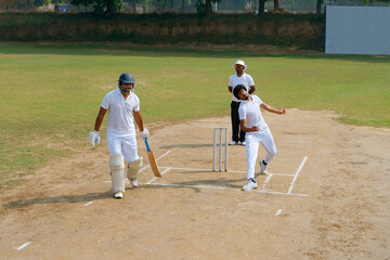 A cricket bowler in full motion, delivering a fast ball on a well-maintained pitch, with an umpire observing