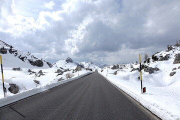 Strada innevata sul Passo Valparola nelle Dolomiti, Italia, con cime montuose e cielo nuvoloso drammatico