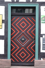 Porta antica in legno con decorazioni geometriche rosse e turchesi in un edificio a graticcio
