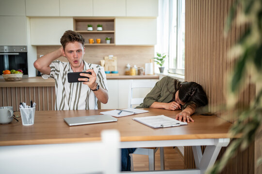 Young man watching videos on smartphone while partner sleeps at table
