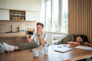 Shocked freelancer reading bad news on smartphone while colleague sleeping at table