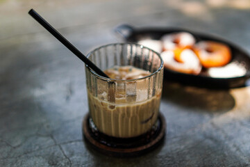 A refreshing iced latte with a black straw stands ready to invigorate, coupled with blurred donuts adding a touch of sweetness, isolated against a serene white backdrop, ideal for promotions.