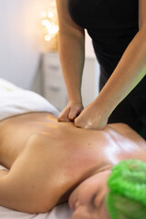 Massage therapist using fists to apply deep pressure on client’s upper back in a wellness session